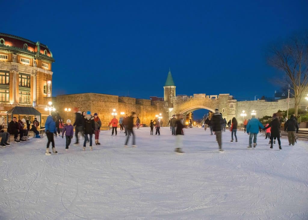 People ice skating at night in old quebec with city walls in background.