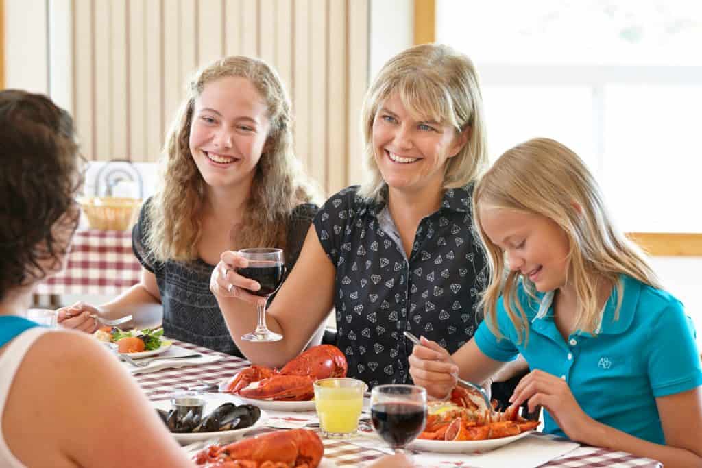 prince edward island - family-lobster supper - woman and girls with plates of lobster at table with checked cloth.