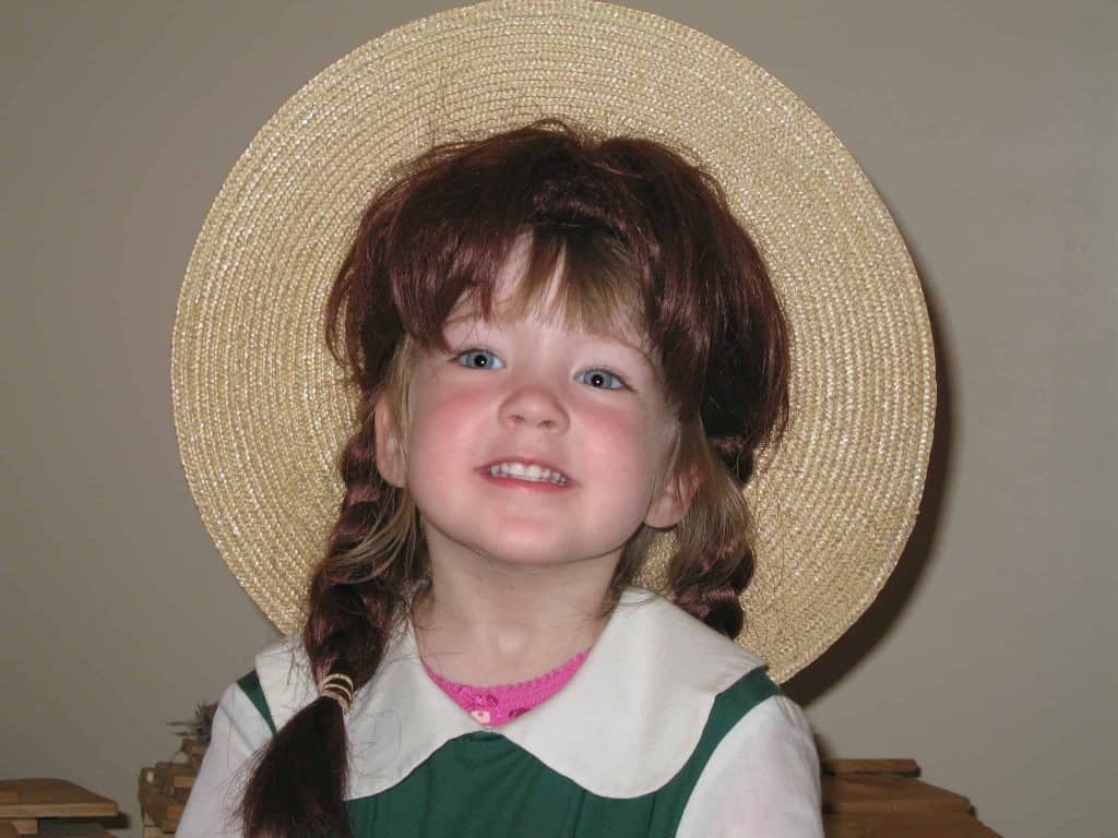 Young girl dressed as Anne of Green Gables with green and white dress, red wig with braids and straw hat.
