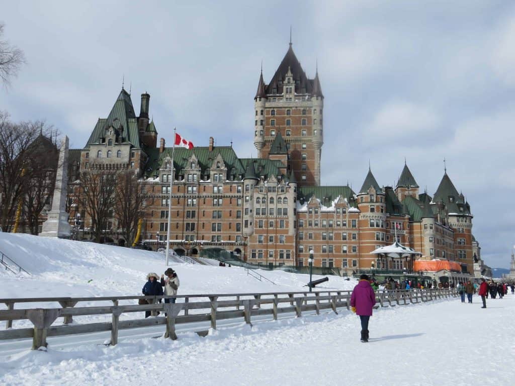 People strolling on Terasse Dufferin in front of Chateau Frontenac in Quebec City in winter with snow on the ground.