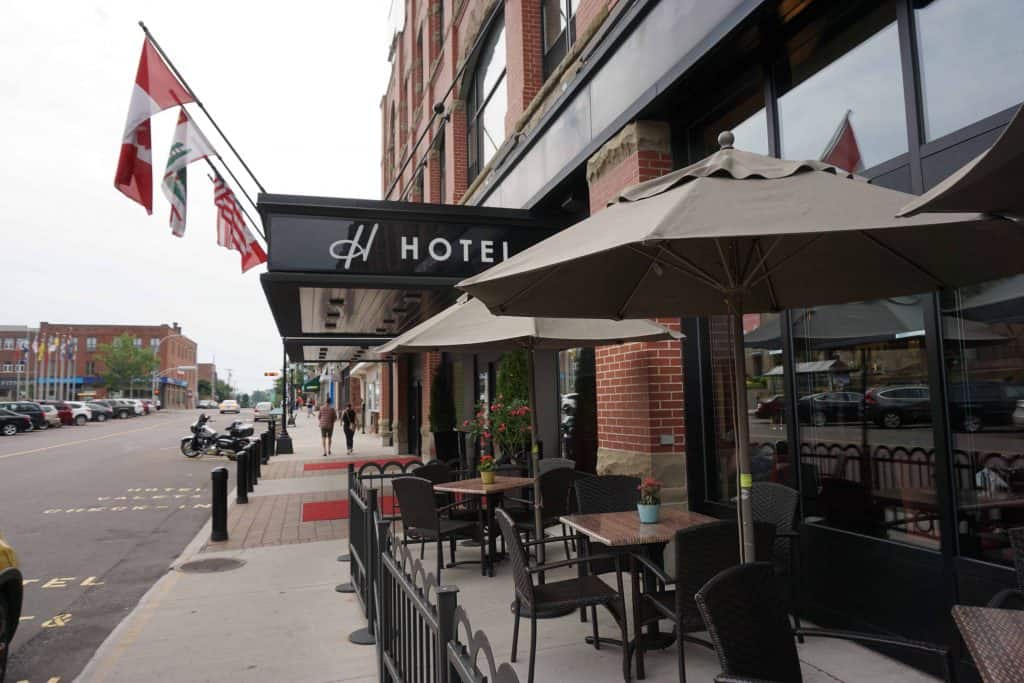 Exterior of the Holman Grand Hotel in Charlottetown, Prince Edward Island with patio umbrellas, tables and chairs on sidewalk outside hotel entrance.