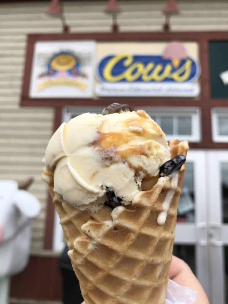 Ice cream cone held up in front of Cows ice cream sign in background.