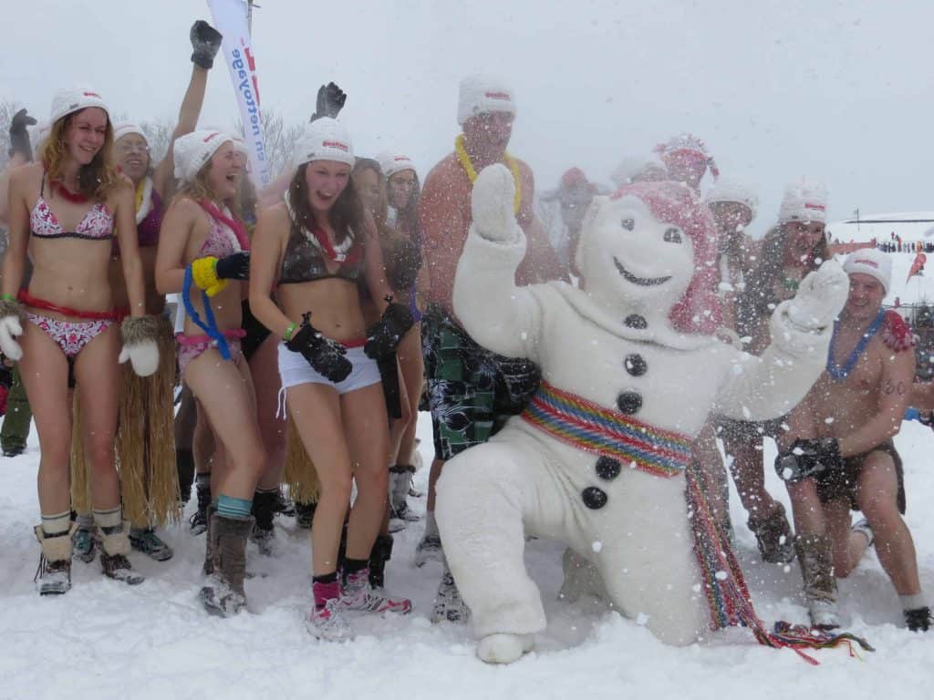 Group of laughing people in bathing suits, hats and mittens posing in snow with Bonhomme at the quebec carnival ice bath in Quebec City.