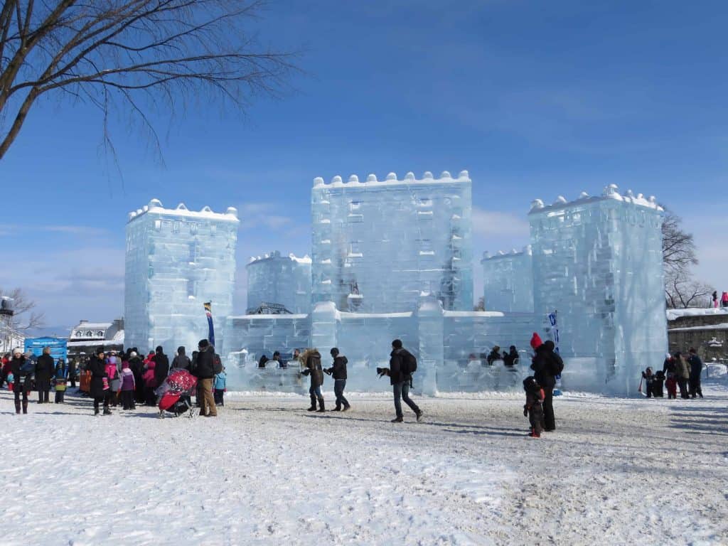 Bright blue sky and crowds of people walking outside an ice palace at the quebec winter carnival in Quebec City.