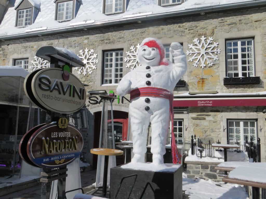 Sculpture of Bonhomme ( a large snowman wearing a toque and arrow sash tied around waist) outside a restaurant on grande allee in quebec city.