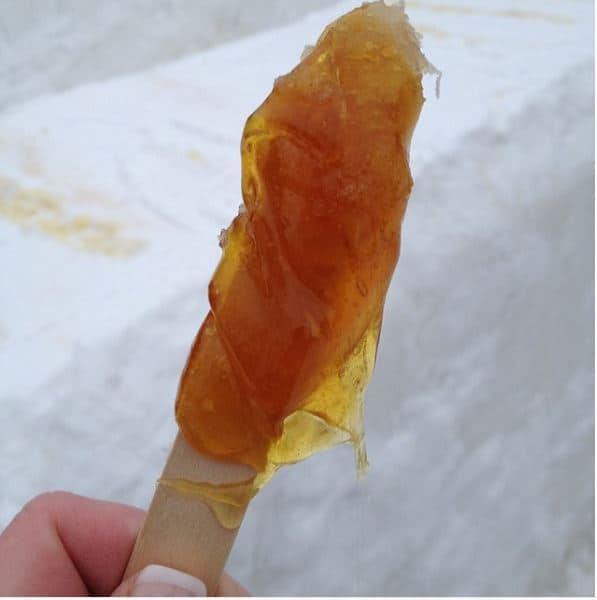 maple taffy on stick held over blocks of snow