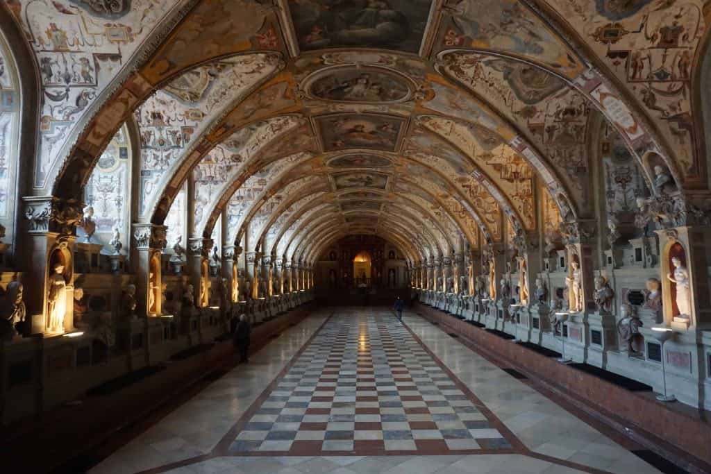 The Munich Residenz Antiquarium - a long hallway with checkerboard flooring, curved ceiling with painted panels, statues displayed along perimeter.