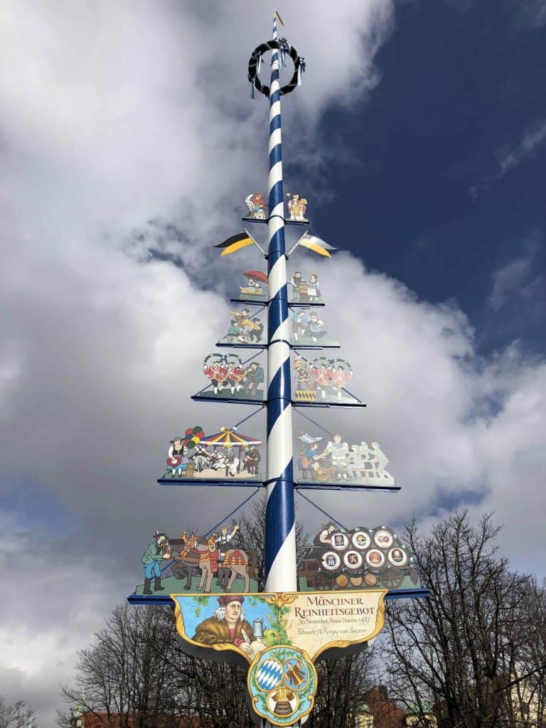 Blue and white striped maypole with symbols of market scenes in Viktualienmarkt in Munich, Germany.