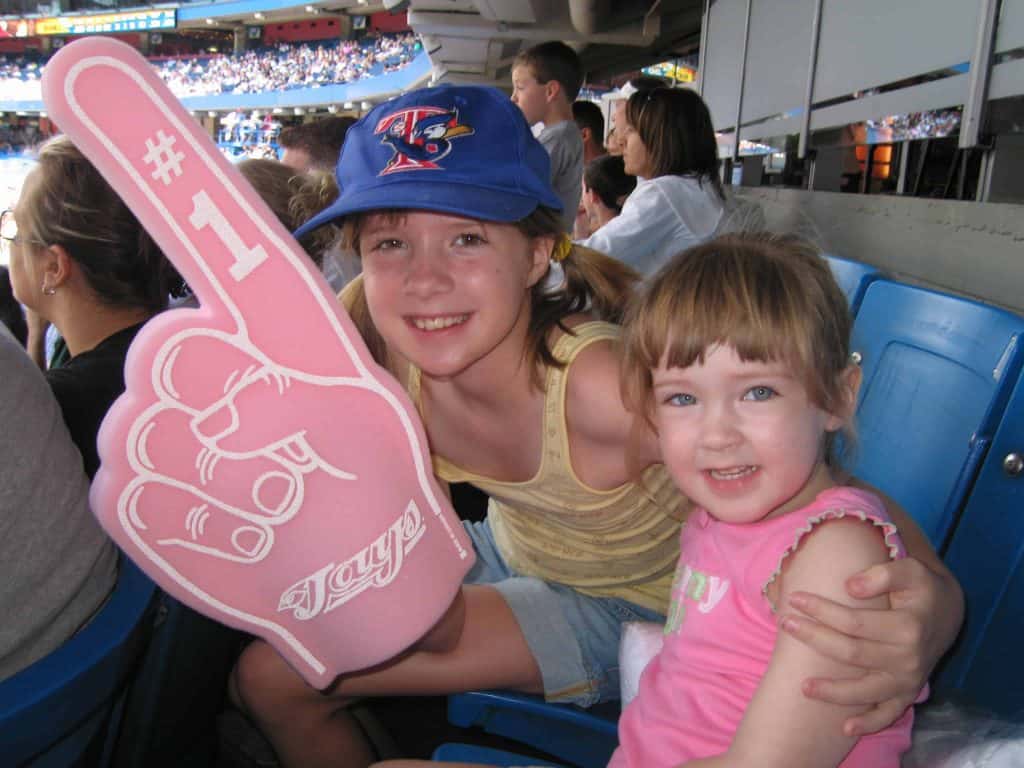 Two young girls at a Blue Jays game holding a pink foam Blue Jays #1.