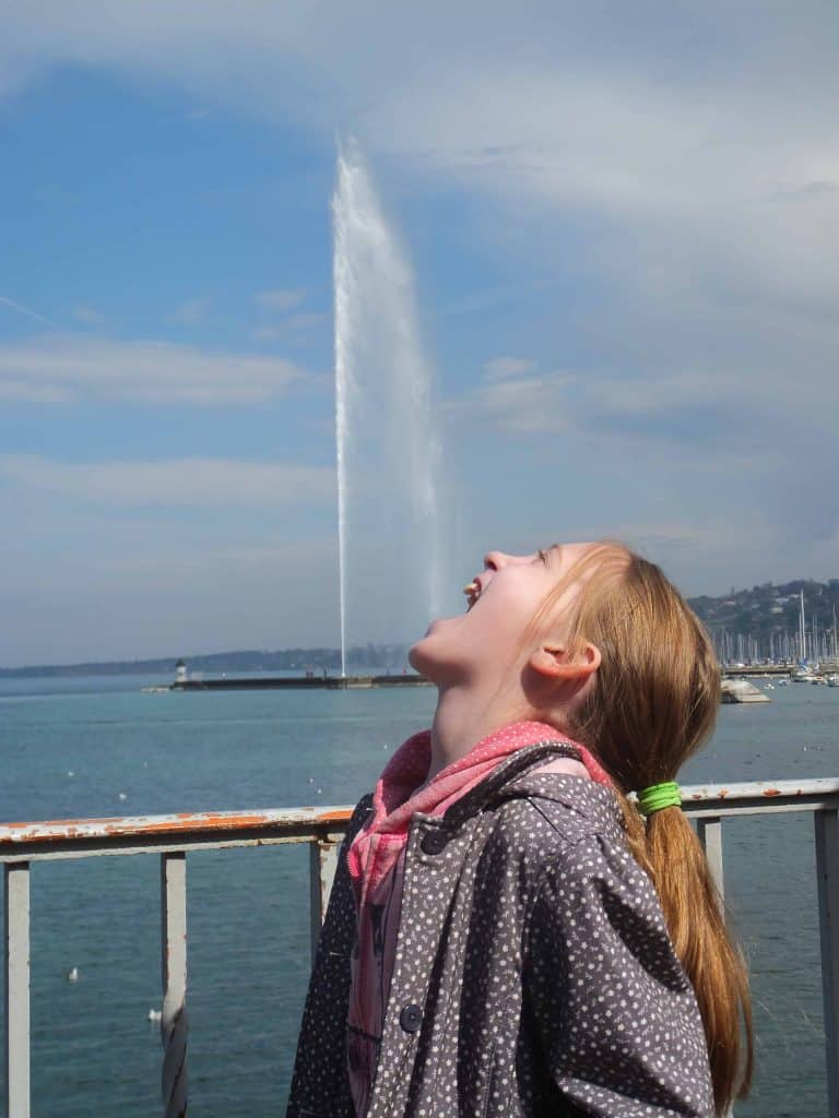 Young girl posing with jet d'eau in Geneva, Switzerland so it looks like she's drinking the water spray.