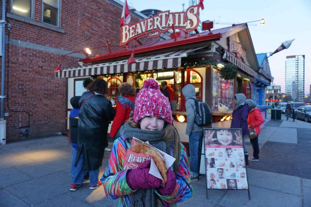 Young girl dressed in winter coat and hat holding a pastry outside BeaverTails in ByWard Market in Ottawa, Canada.