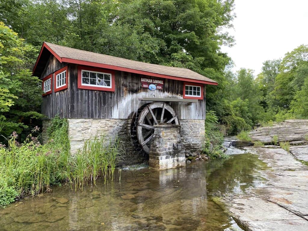 Batman Sawmill in Sheguiandah on Manitoulin Island - weathered wood and stone building with red trim and waterwheel alongside water.