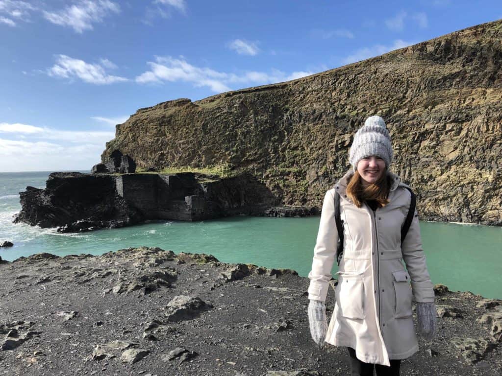 Teen girl in light coloured coat, gray hat and mittens standing by Pembrokeshire's Blue Lagoon.