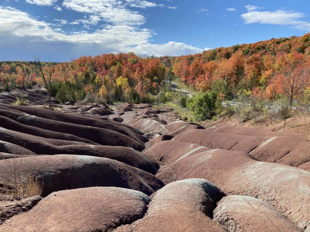 Cheltenham Badlands in Caledon, Ontario with fall trees in background and blue sky with a few clouds.
