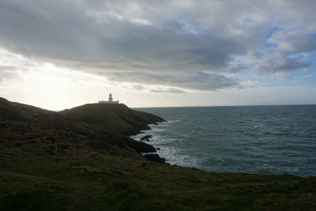 Strumble Head Lighthouse in distance at dusk.
