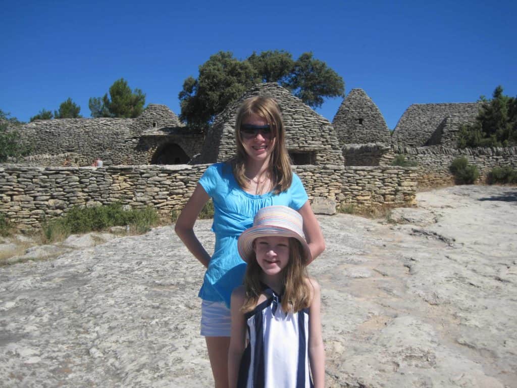 Teen girl and younger girl in hat in front of borie structures at Village des Bories in Gordes, France.