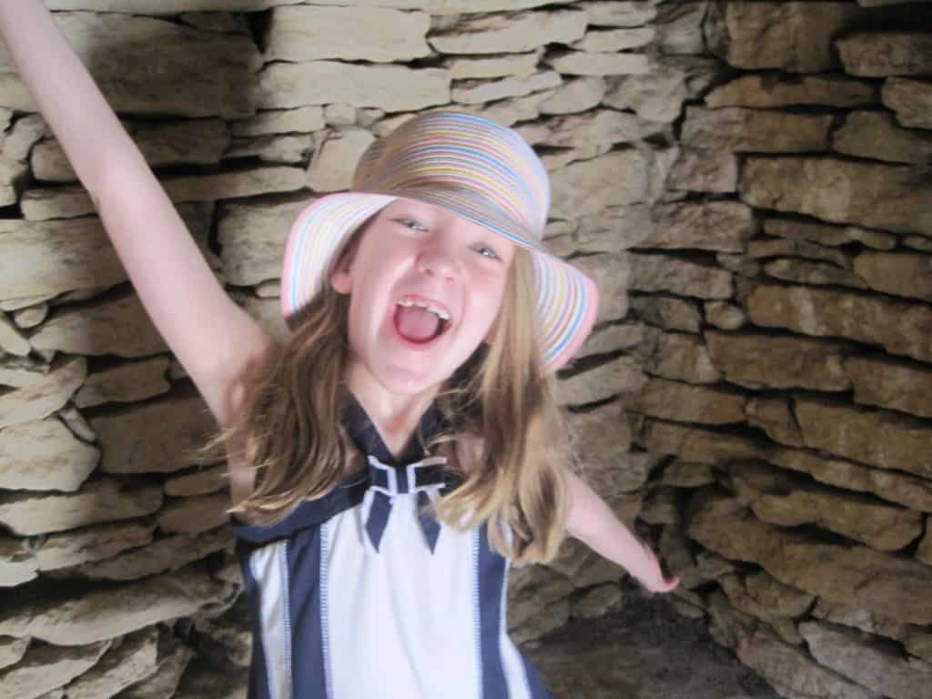 Young girl with arms outstretched and laughing inside borie structure at Village des Bories.