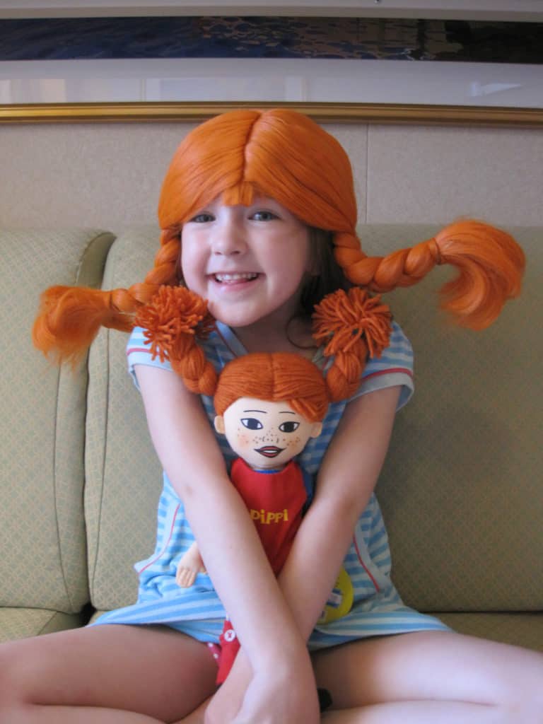 Young girl in blue striped dress wearing Pippi Longstocking wig and holding Pippi doll.