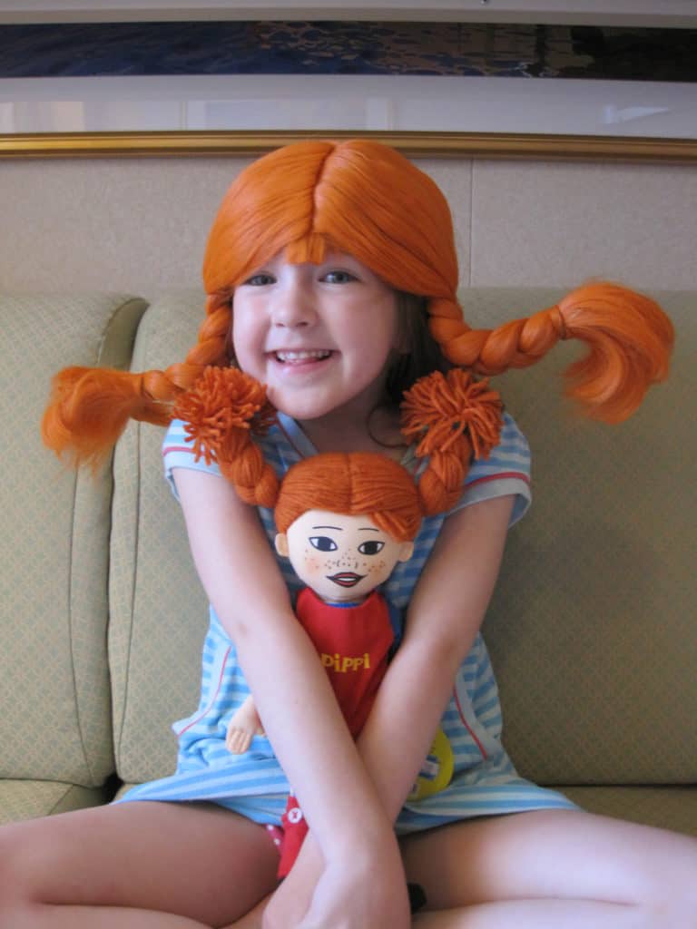 Young girl wearing Pippi Longstocking wig and holding Pippi Longstocking rag doll.