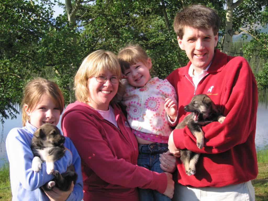 Mom, dad and two young girls holding sled dog puppies in Alaska.