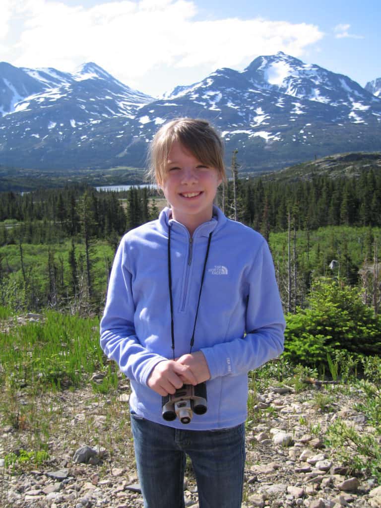 girl in blue sweater carrying binoculars-near skagway alaska-mountains in background