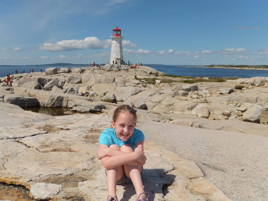 young girl sitting on rocks at peggy's cove with lighthouse in background.