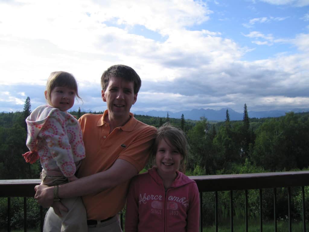 Young girl standing beside man holding smaller girl on patio at Princess Mt. McKInley Lodge.