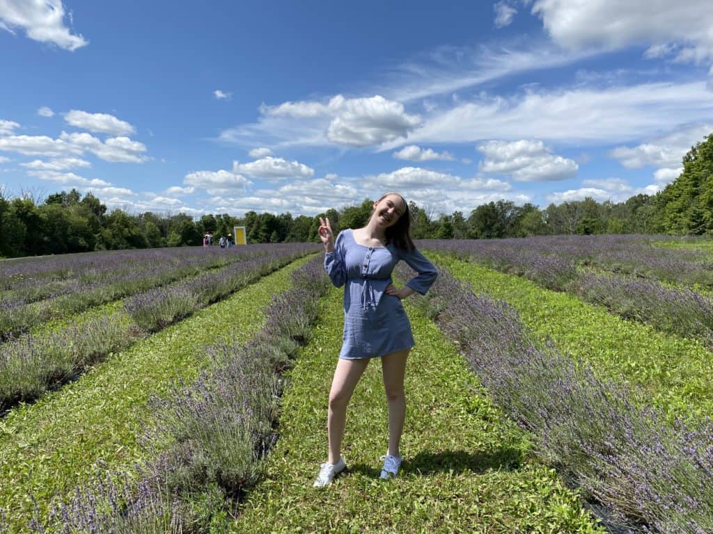 Young woman posing in fields at Terre Bleu Lavender Farm with yellow door in background.
