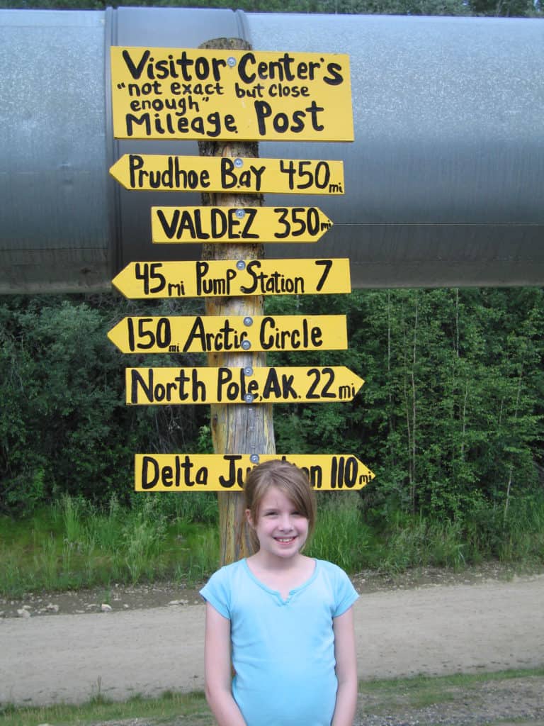 young girl with mileage sign post at trans alaskan pipeline, fairbanks, alaska.
