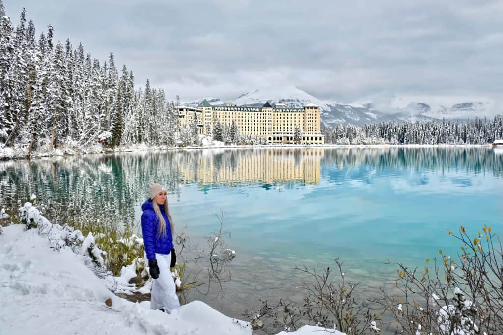 Young woman in ski clothing by lake with Chateau Lake Louise in background.
