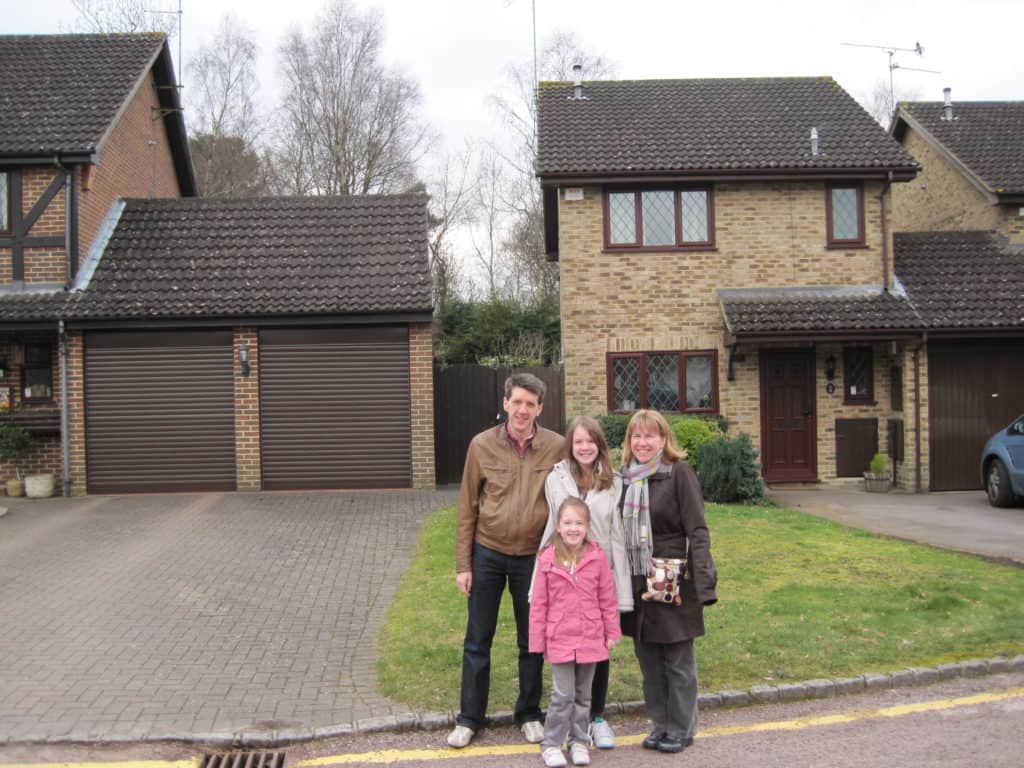 Family of mom, dad, teen girl and younger girl standing outside brown brick house used as no. 4 privet drive in harry potter films.