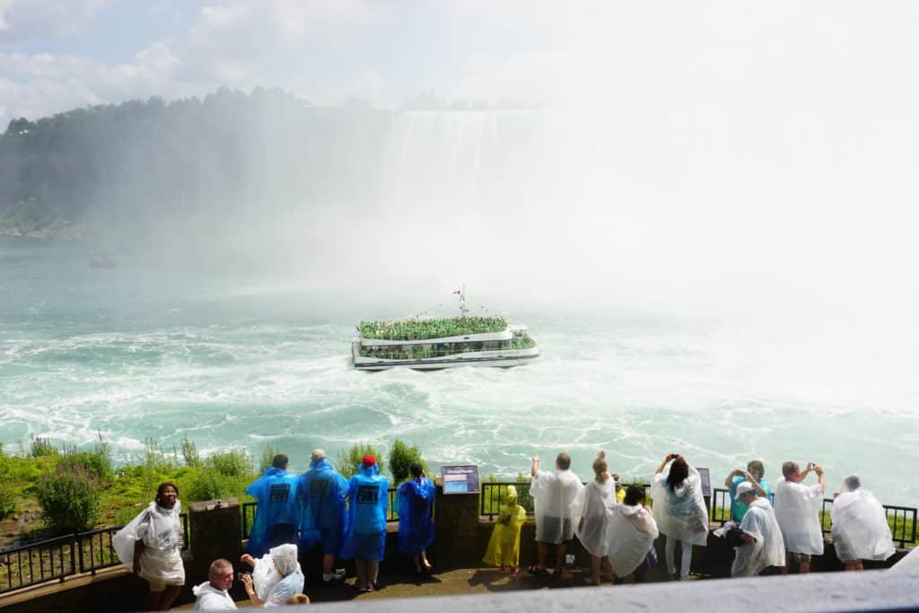 Group of people on observation deck taking photos of boat sailing into basin of Niagara Falls, Canada.