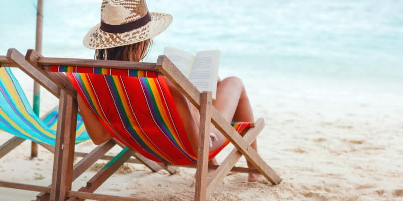 Woman sitting in striped chair reading book on beach