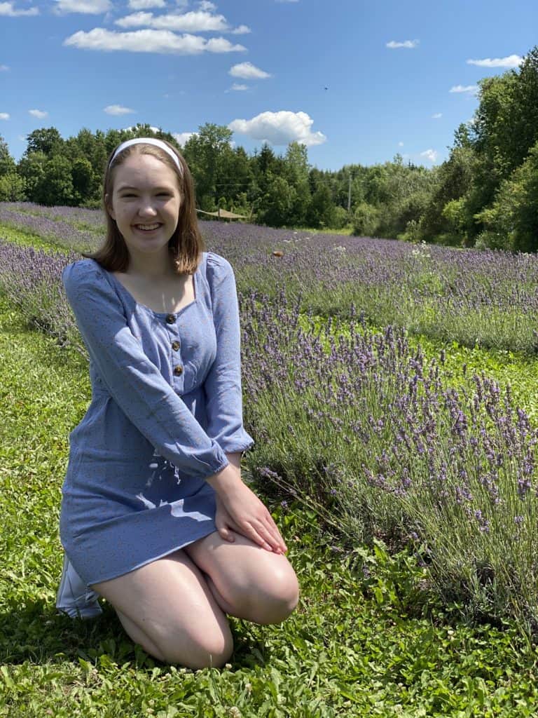 Young woman kneeling in fields of lavender plants at Terre Bleu Lavender Farm.