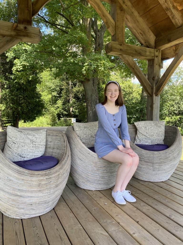 Young woman sitting on wicker chairs with purple cushions in gazebo at Terre Bleu Lavender Farm.