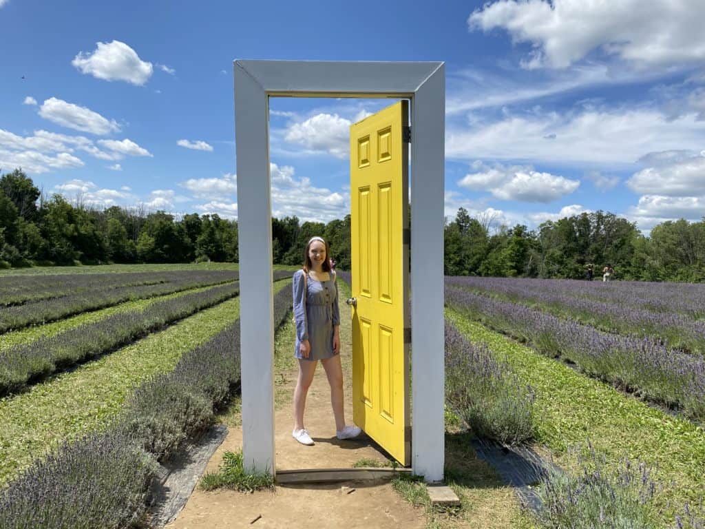 Young woman by yellow door in lavender fields at Terre Bleu Lavender Farm.
