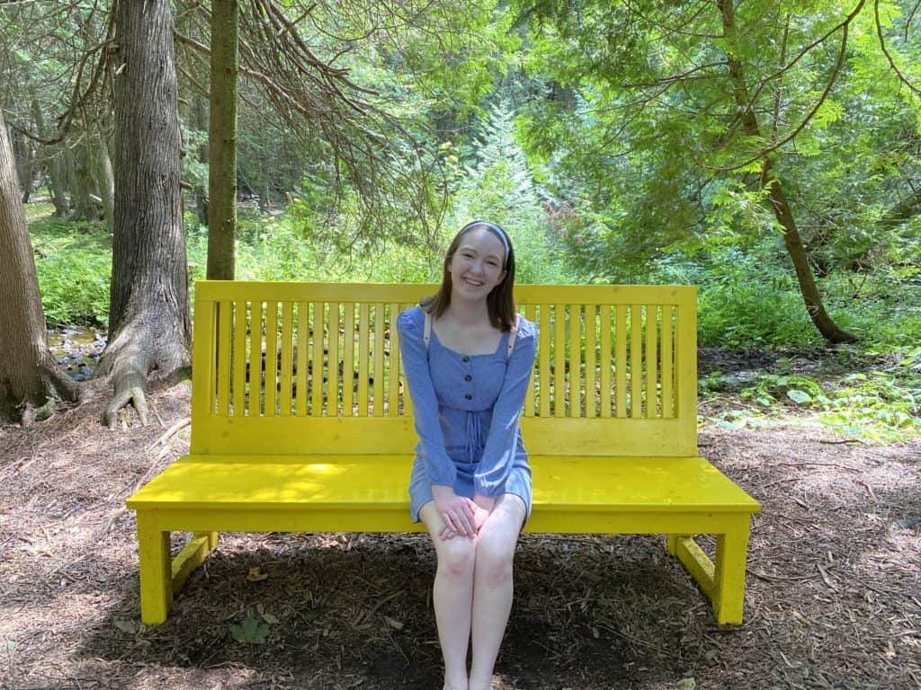 Young woman sitting on yellow bench in the forest at Terre Bleu Lavender Farm.