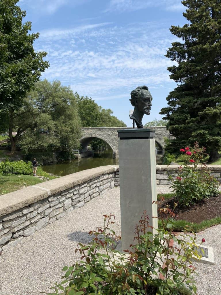 Bust of man's head on piller in Shakespearean Gardens with river and bridge in background - Stratford, Ontario.