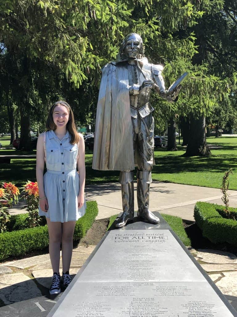 Young woman in blue dress standing beside statue of William Shakespeare at Stratford Festival in Stratford, Ontario.