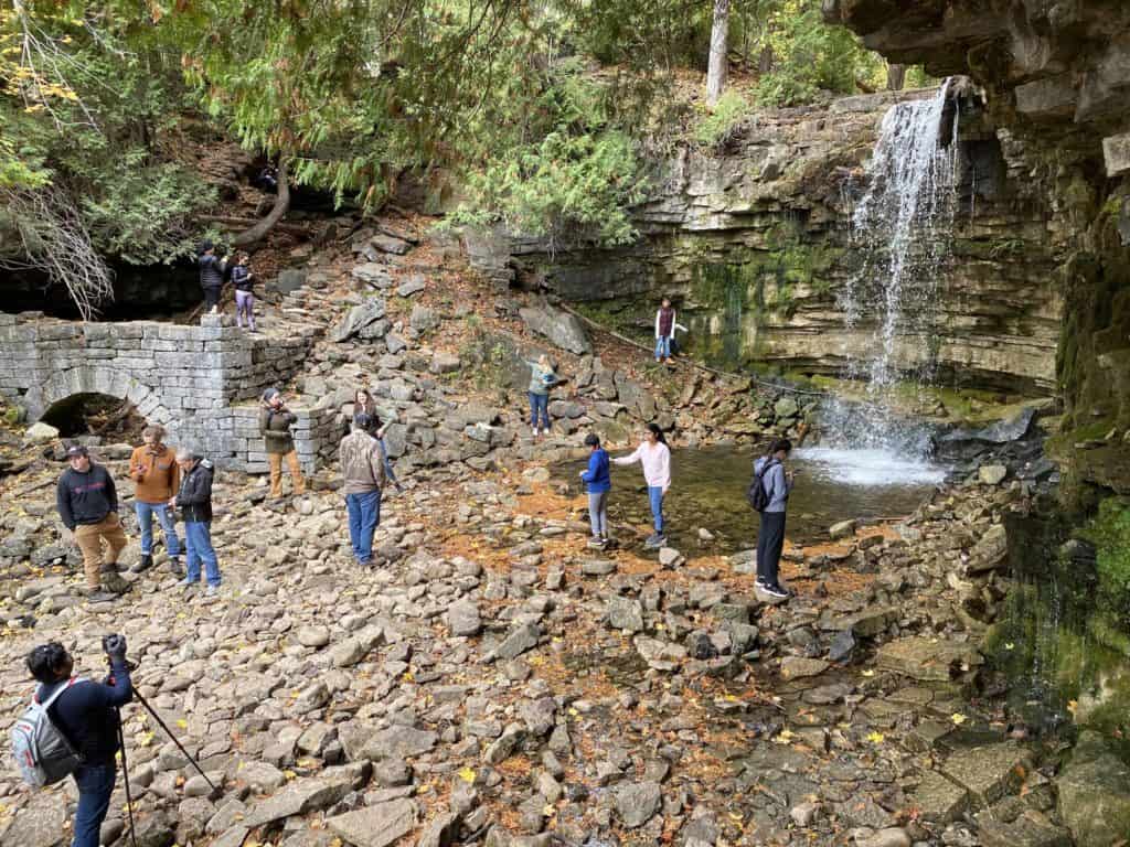 People standing around Hilton Falls - orange leaves on ground on a fall day.