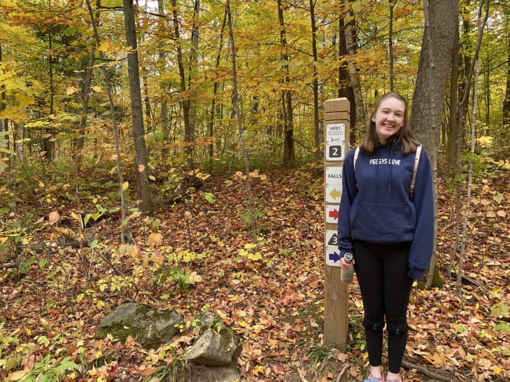 Young woman hiking at Hilton Falls Conservation Area standing next to trail marker.