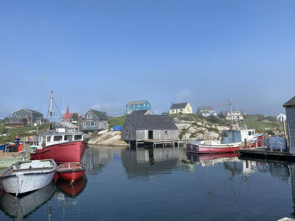 Red and white boats in harbour at Peggy's cove reflected in water with buildings on rocks in background.