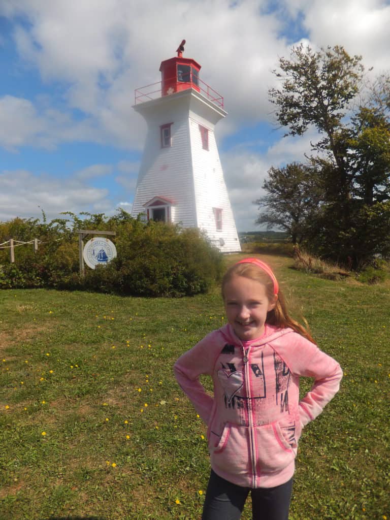 Young girl in pink sweatshirt by the lighthouse in Victoria-by-the-Sea, Prince Edward Island.