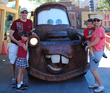 Man and woman with boy and girl posing with one of the Cars at Disneyland.