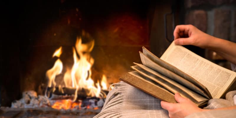 hands of woman reading book by fireplace