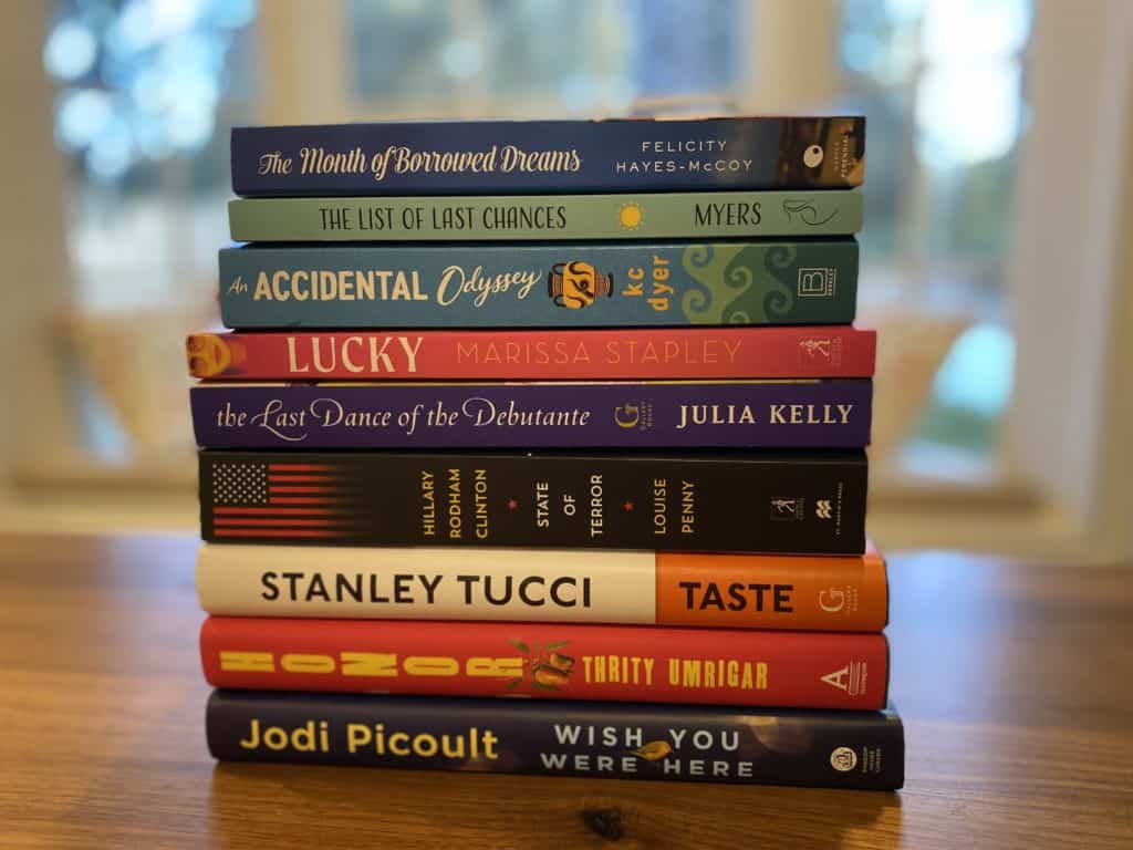 Stack of books on table in front of window.