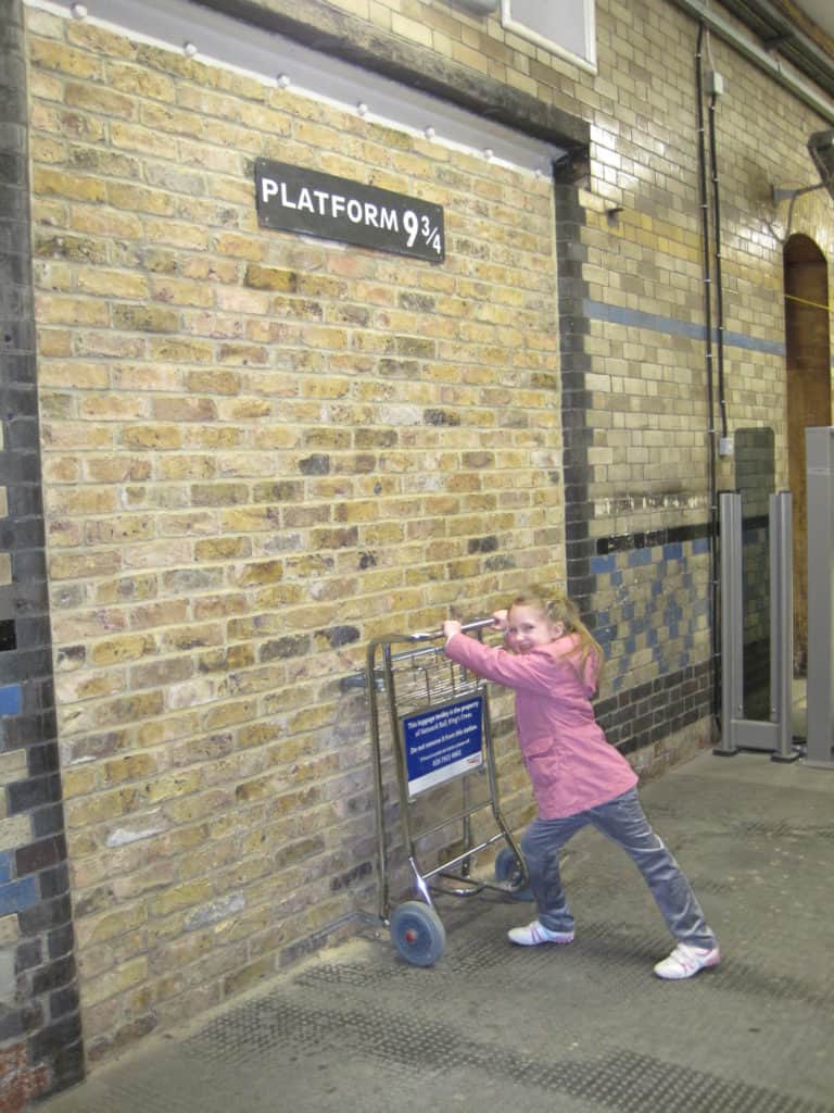 Young girl pushing Harry Potter cart at King's Cross station in London, England.
