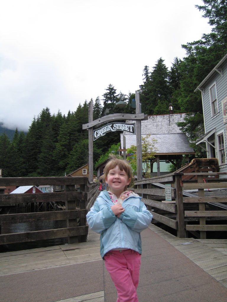 Young girl in pink pants and blue rain jacket at entrance to Creek Street in Ketchikan, Alaska.