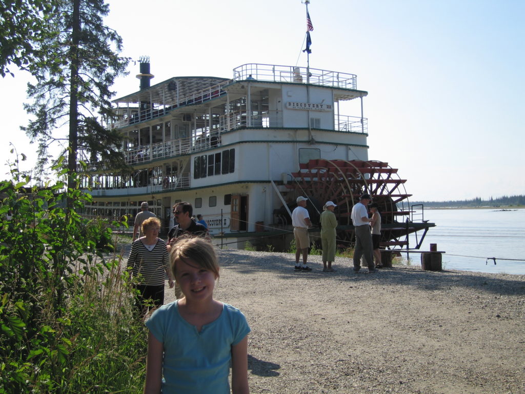 Young girl standing near paddlewheel riverboat in Fairbanks, Alaska.