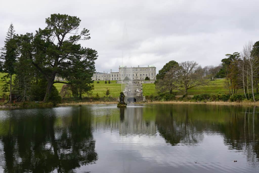 Powerscourt Gardens, Ireland - trees around pool with small fountain and grand home in background - all reflected in water.